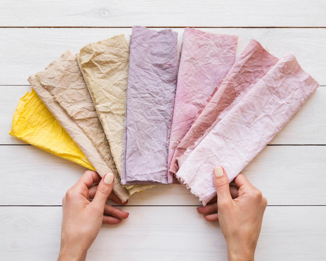 Hands holding pastel-dyed fabric swatches made with Kadam Colors’ eco-friendly dyes for sustainable and creative textile projects.