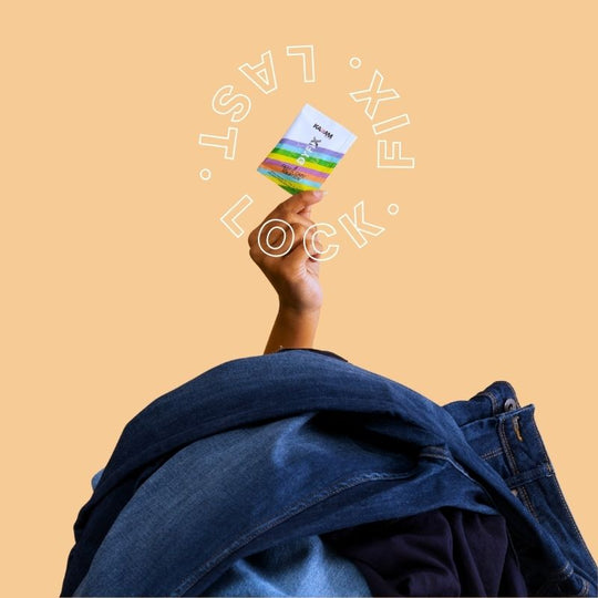 Hand rising from a pile of jeans holding Kadam Colors DyFix sachet with “LOCK. FIX. LAST.” text circling it.