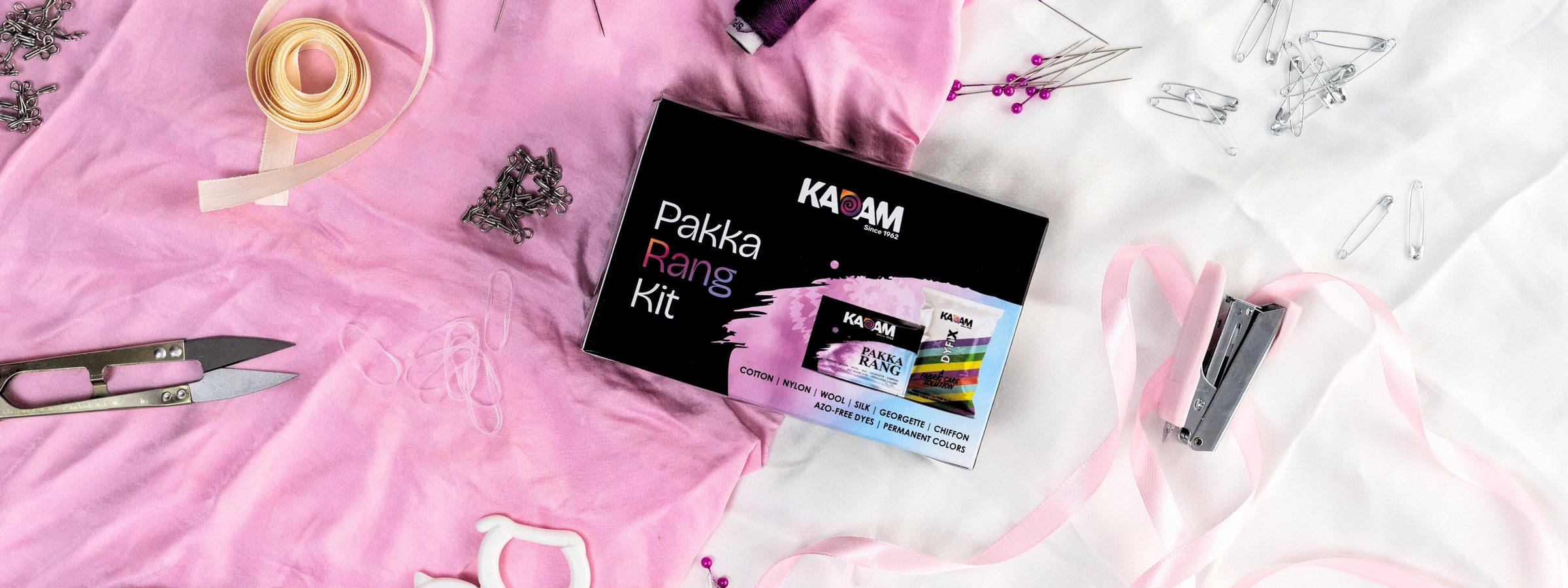 Creative flatlay of Kadam Colors Pakka Rang Kit surrounded by tailoring tools and accessories on pink and white background