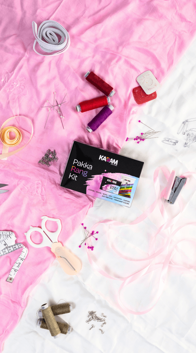 Flatlay of Kadam Colors Pakka Rang Kit with threads, pins, scissors, and sewing supplies on pink and white fabric.