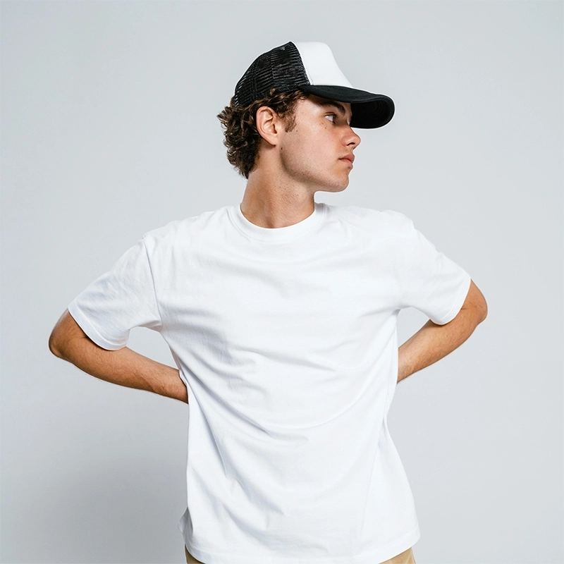 Male model in a white t-shirt and black cap posing with hand on hip – Kadam Colors product demo shot.