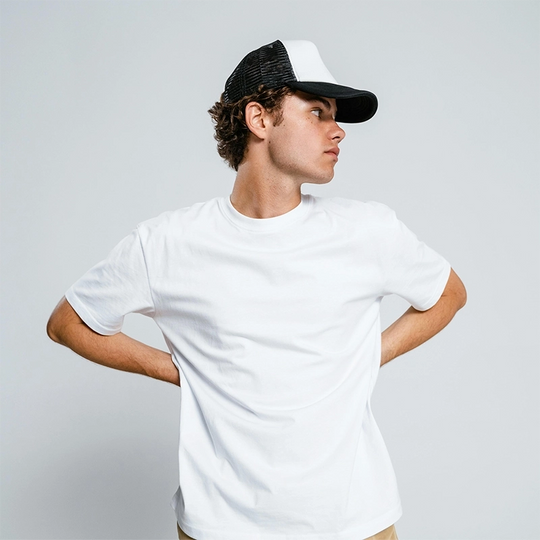 Male model in a white t-shirt and black cap posing with hand on hip – Kadam Colors product demo shot.