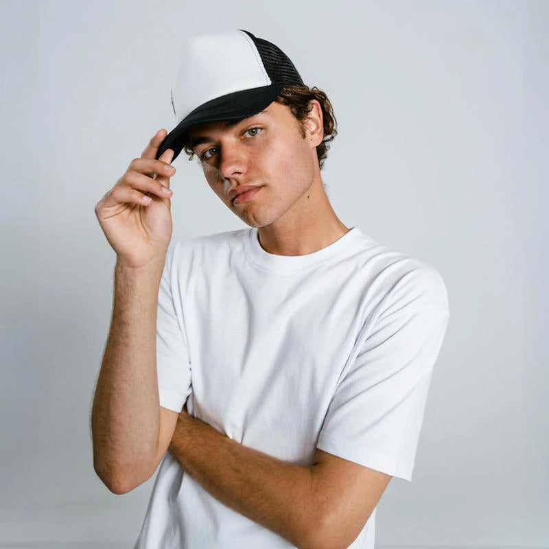 Male model in white t-shirt tipping his black cap – minimal look ready for Kadam Colors fabric dye use.