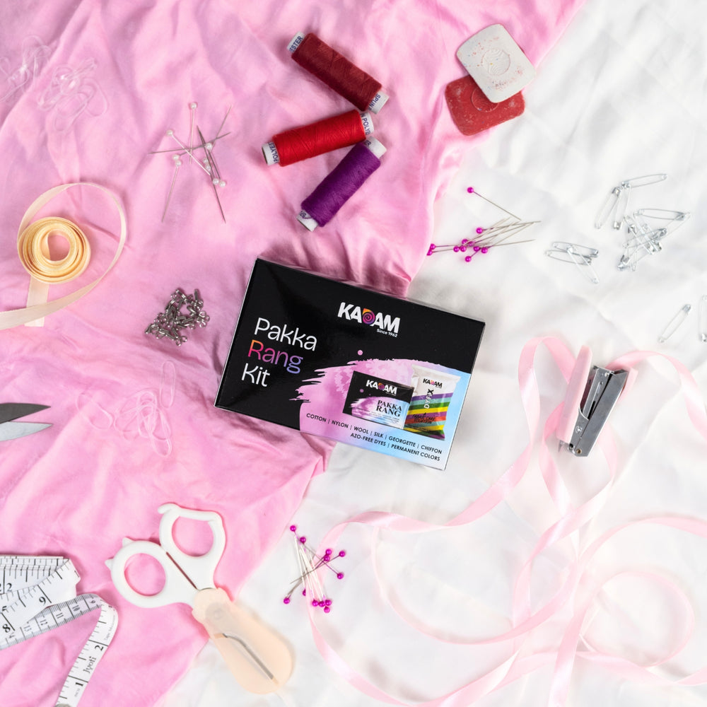 Kadam Pakka Rang Kit placed on pink fabric with sewing essentials like threads, ribbons, scissors, and pins for fabric dyeing projects.