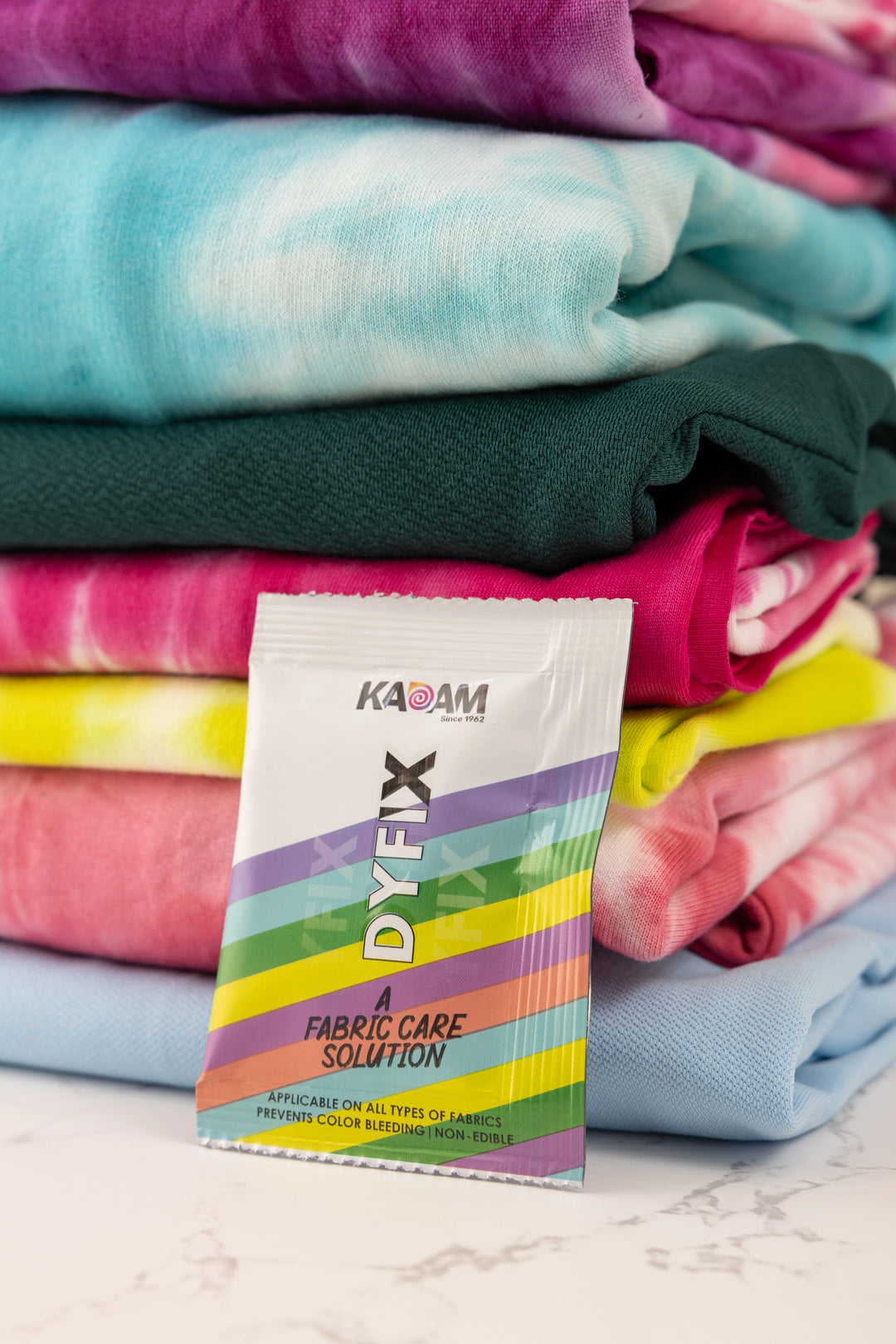 Kadam DyFix sachet placed in front of colorful tie-dye fabrics—prevents color bleeding and keeps clothes vibrant after dyeing.