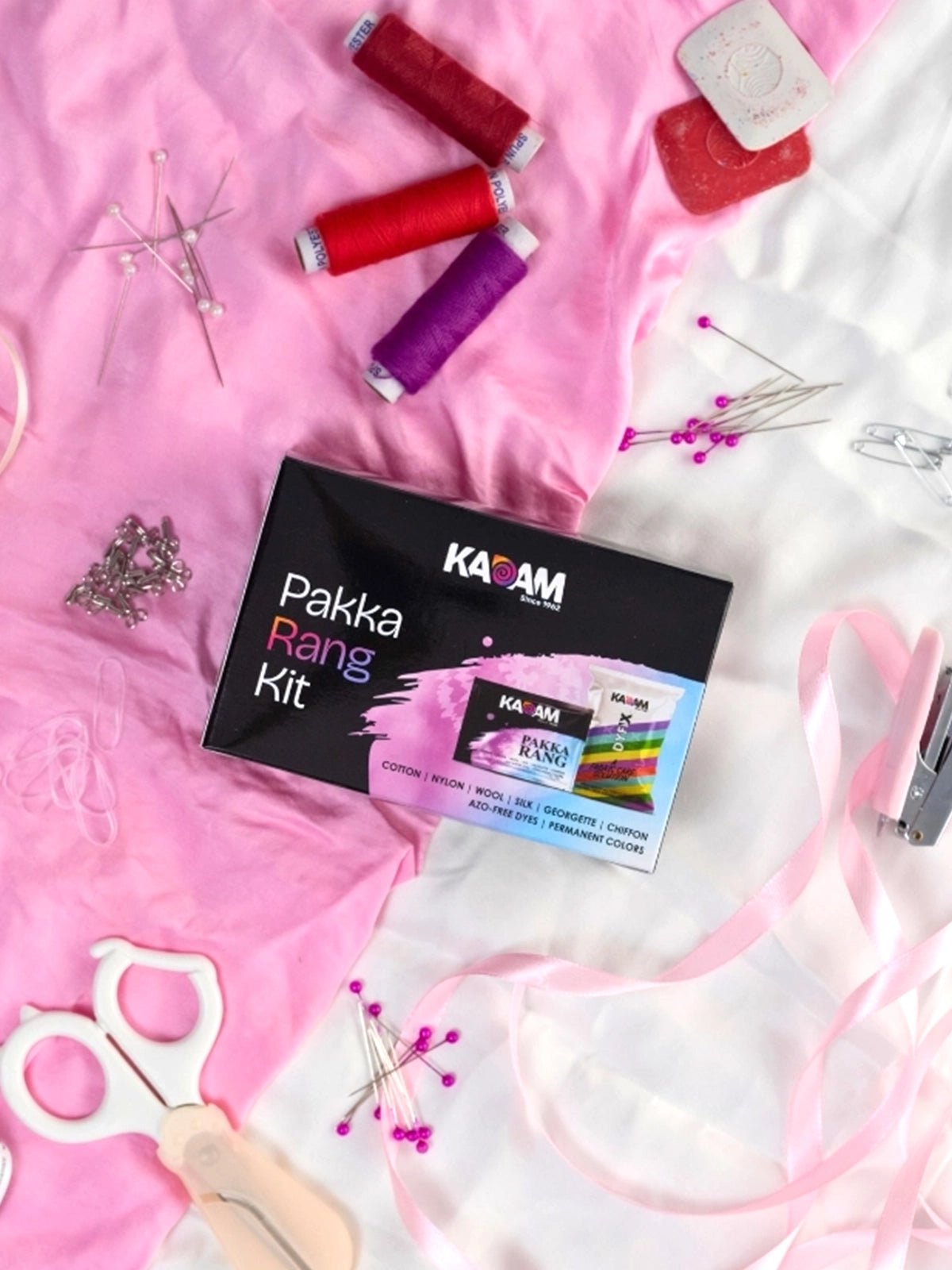 Kadam Pakka Rang fabric dye kit placed on pink fabric with sewing tools, permanent azo-free dye for cotton, silk, wool and DIY clothing projects.