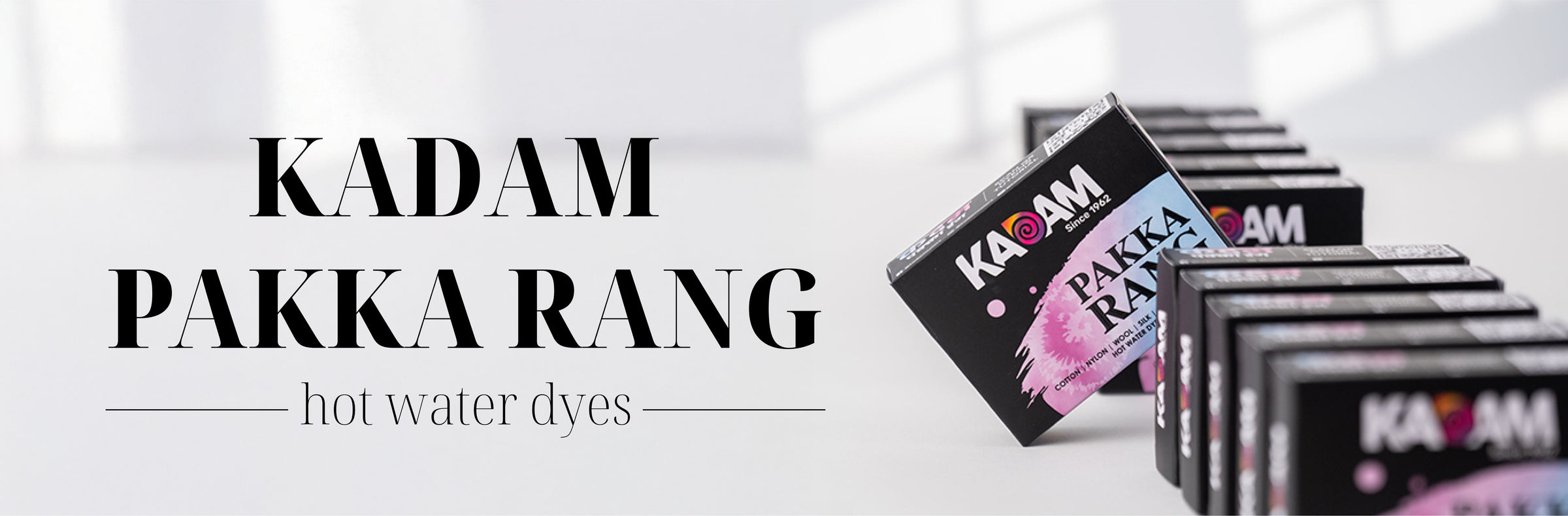 Kadam Pakka Rang hot water dyes in sleek black packaging, arranged in a neat row on a white surface with soft light and shadows, emphasizing the premium quality and vibrant color results of the product