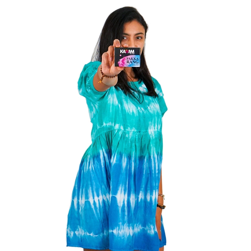 Woman wearing a blue and green tie-dye dress holding a Kadam Pakka Rang product.