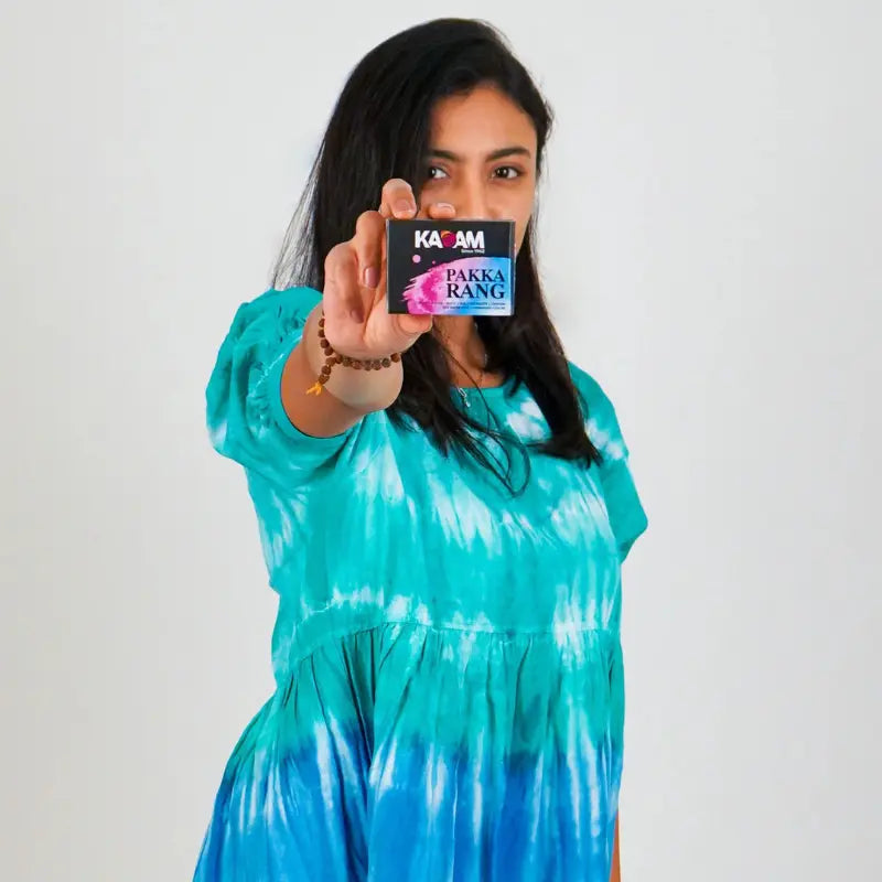 Woman in turquoise tie-dye dress holding Kadam Pakka Rang fabric dye for bold and lasting fabric colors.