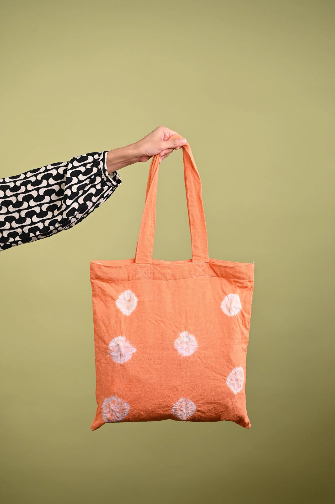 Hand holding a vibrant orange tote bag with white tie-dye prints, dyed using Kadam Colors.