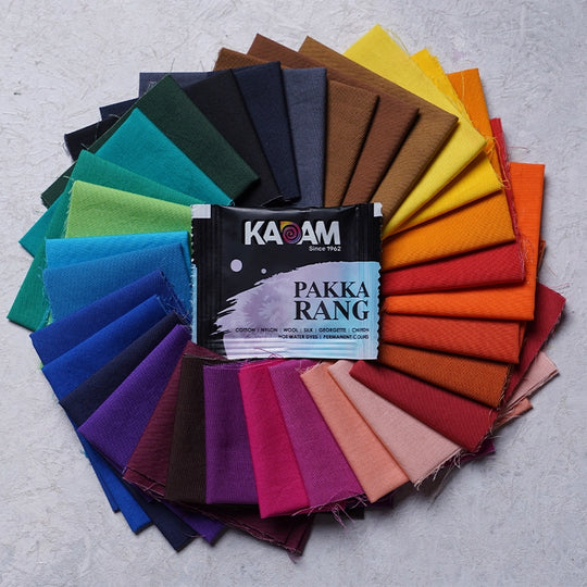 Kadam Pakka Rang fabric dye sachet displayed with a vibrant circular arrangement of dyed fabric swatches in various colors, showcasing the wide range of hues achievable with the high-quality dyes.